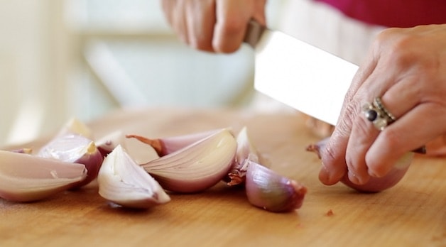 Cutting shallots into quarters on a cutting board
