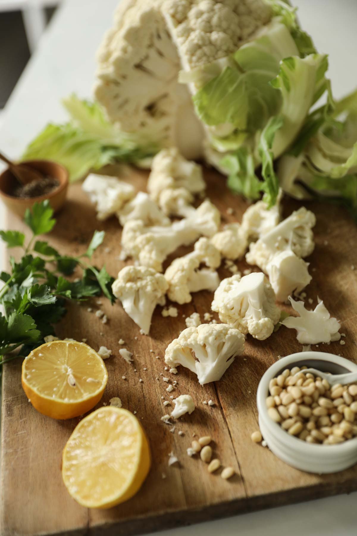 Cauliflower, lemon, pinenuts and parsley on a cutting board.