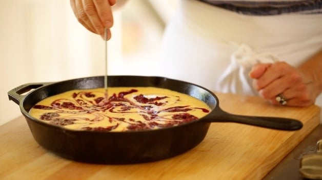 a person using a long skewer to swirl blackberry puree into cornbread batter