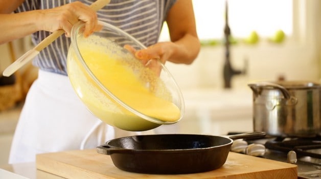 Cornbread batter being pouring into a cast-iron skillet