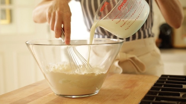 Adding milk to flour in a glass bowl to form a crepe batter
