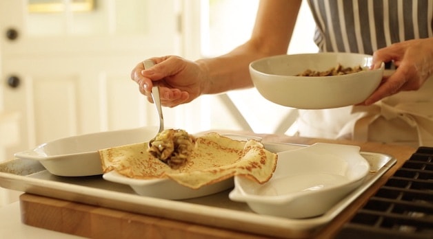 Adding mushroom and leek filling to a crepe in a gratin dish