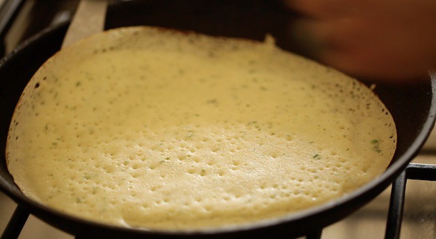 a crepe cooking in a skillet with the edges turning golden brown