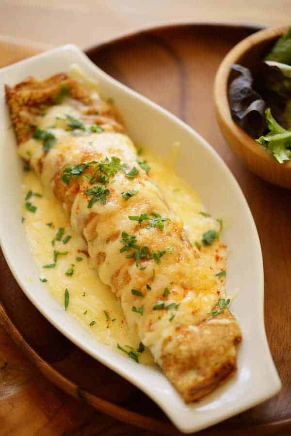 Vertical image of a Baked crepe in a white gratin dish on a wooden charger with small side salad