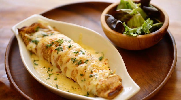 Baked Chicken and Mushroom Crepe in a gratin dish on a wooden charger with side salad in a small olive wood bowl