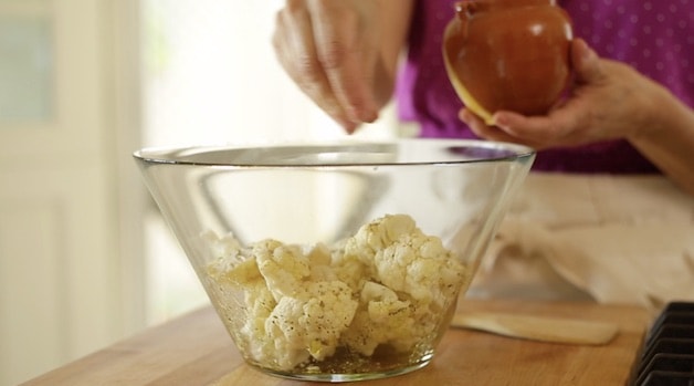 Sprinkling salt and pepper on cauliflower in a bowl