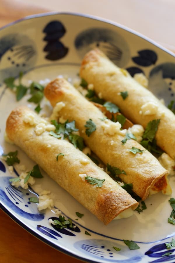 3 taquitos on a plate with queso fresco cheese and cilantro