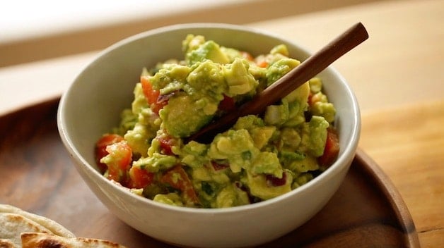 chunky guacomole in a white dish with wooden spoon