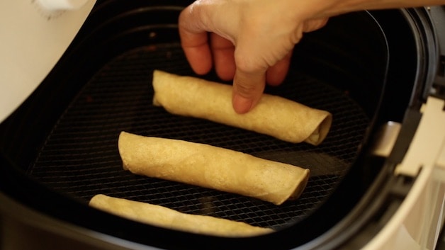 Placing rolled taquitos in an air fryer basket to air fry