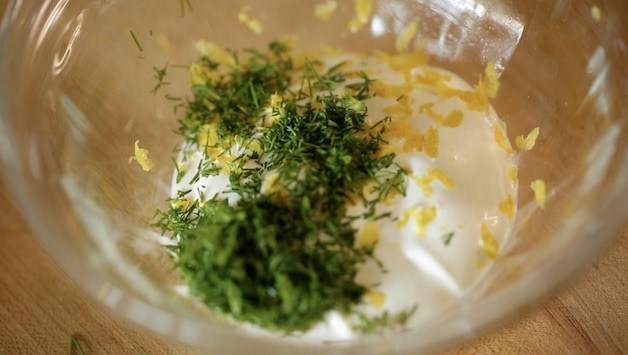 Sour cream in a bowl with minced dill and lemon zest on top