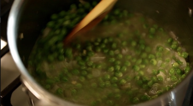 Simmering frozen peas, shallots and chicken broth in a sauce pan