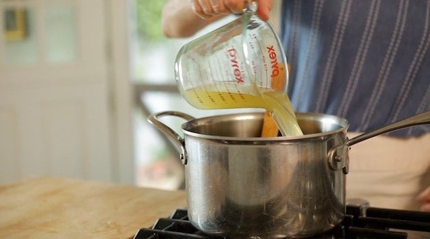 adding chicken broth to a sauce pan