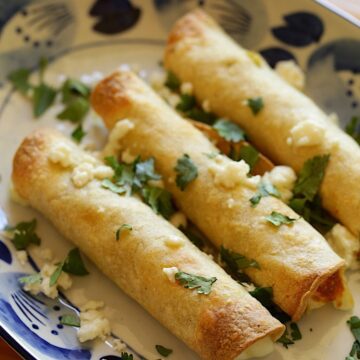 Taquitos on a Blue and White Plate with Cilantro and Cheese