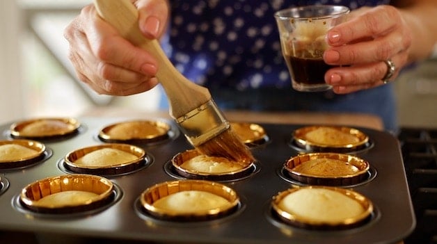 brushing coffee bath onto vanilla cupcakes in a muffin tin