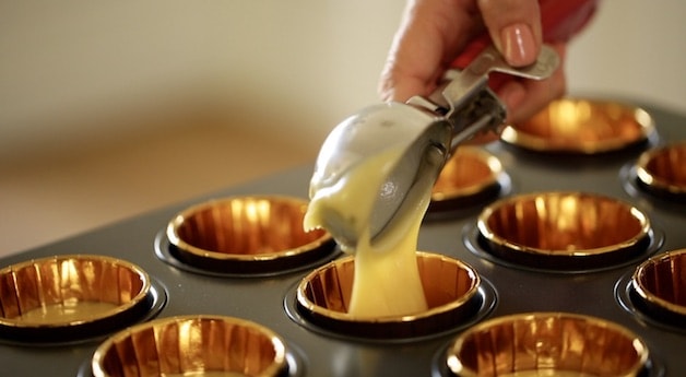 scooping vanilla cupcake batter into a muffin tin