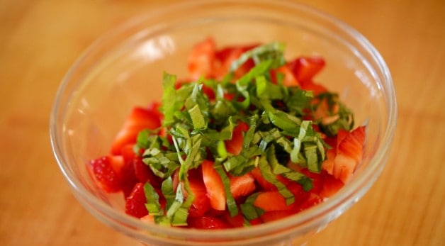 A clear bowl of chopped strawberries and chopped basil