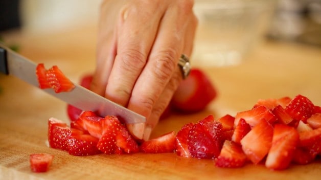 A person chopping strawberries on cutting board