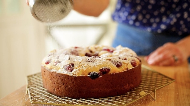 Adding powdered sugar to a raspberry almond cake on a cooling rack