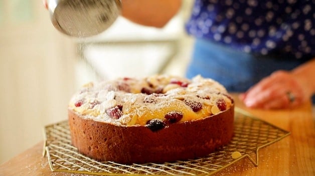 Adding powdered sugar to a raspberry almond cake on a cooling rack