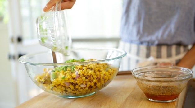 adding Jalapenos to a clear glass bowl filled with corn