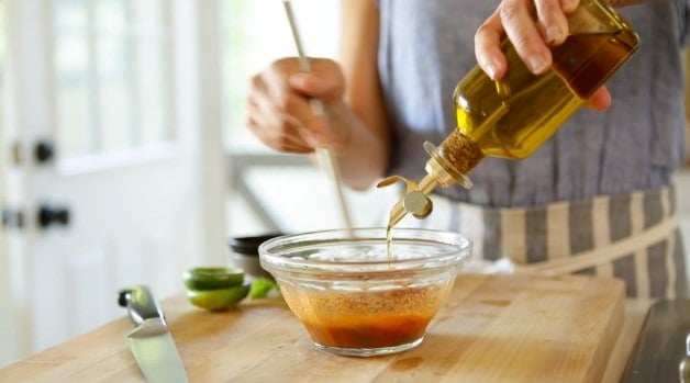 Olive oil being poured in mixing bowl with dressing ingredients