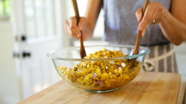 Tossing corn salad in a clear glass bowl