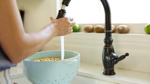 Rinsing corn in a blue colander at the sink