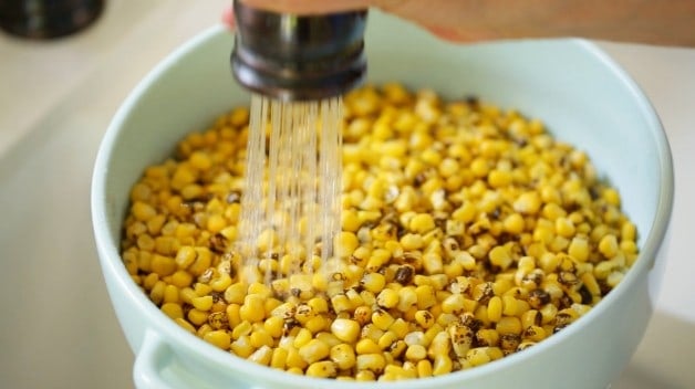 Rinsing charred corn in a blue colander