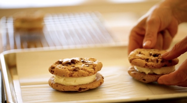 2 ice cream chocolate chip cookie sandwiches on a baking tray lined with parchment paper