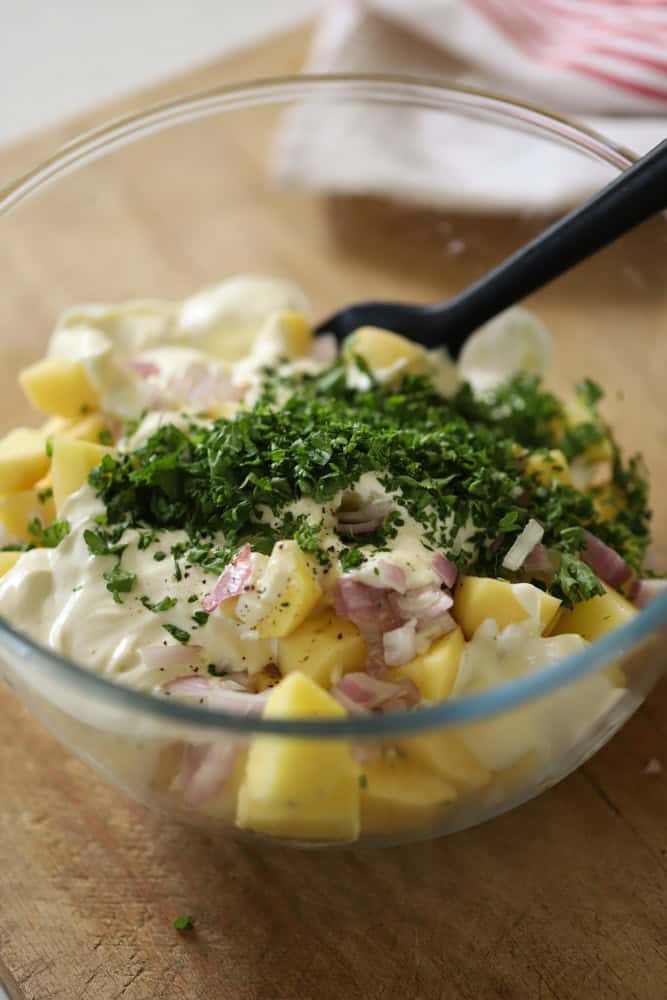 a bowl ofd potatoes covered in dressing, herbs, shallots and seasonings.
