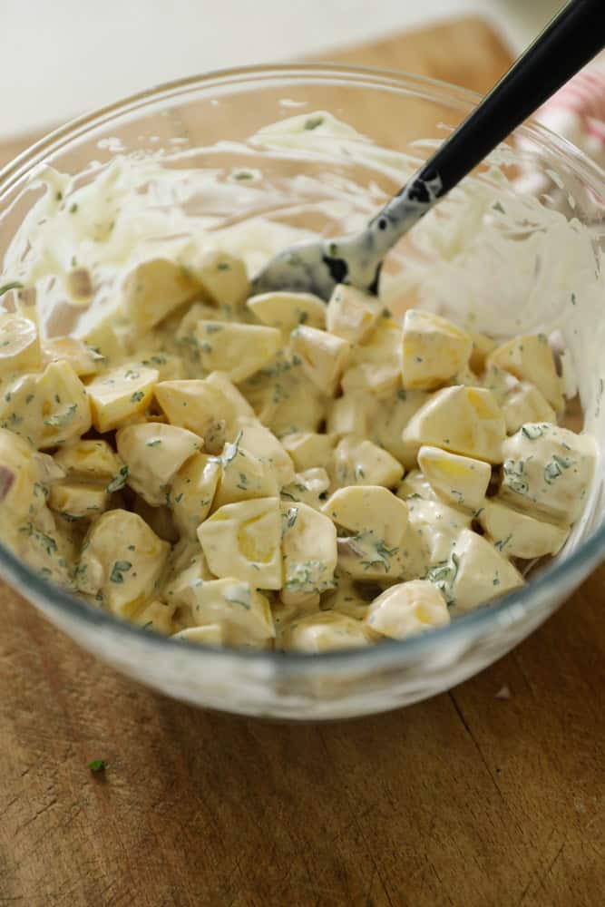 A close up of a potato salad being covered with dressing.