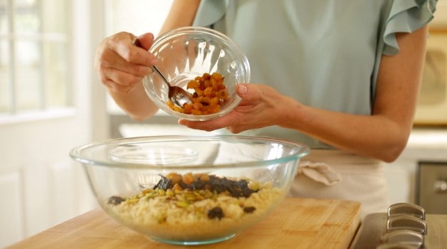 Adding dried fruit to couscous in clear mixing bowl