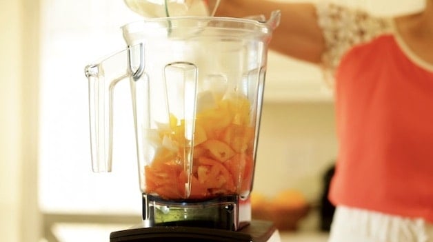 Adding white onion to a blender filled with tomatoes and yellow peppers