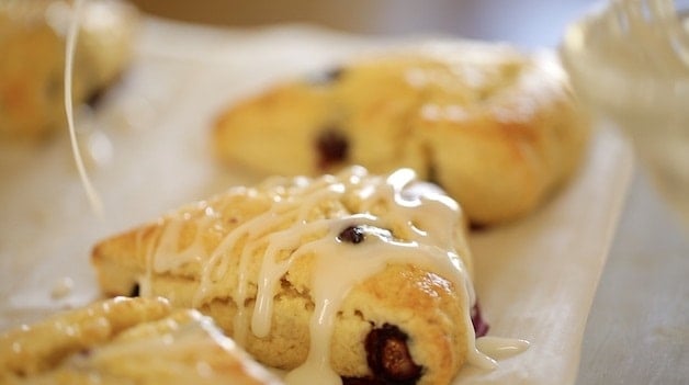 Zitronenglasur über Zitronen-Blaubeer-Scones auf Pergamentpapier träufeln