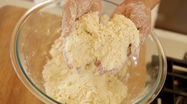 Showing a crumbly scone dough mixture in someone\'s hands as a coarse meal