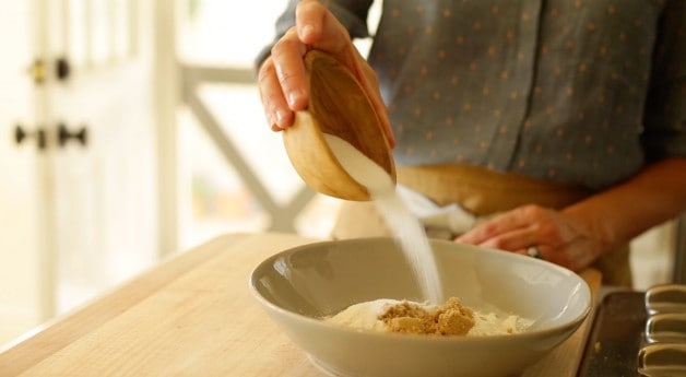 adding sugar to a bowl of crumb topping ingredients 