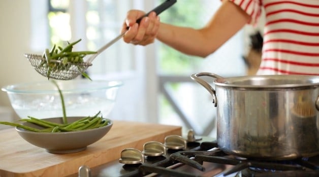 Green beans in a spider strainer about to be blanched in hot water