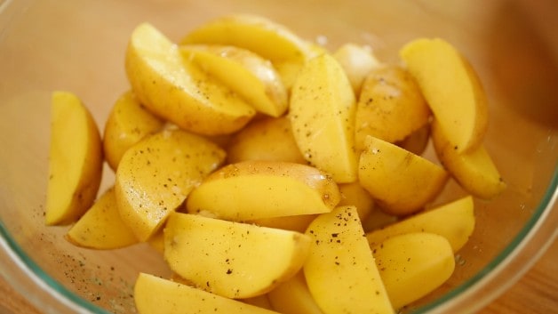 Sliced Yellow Potato Wedges in a bowl with olive oil and seasoning