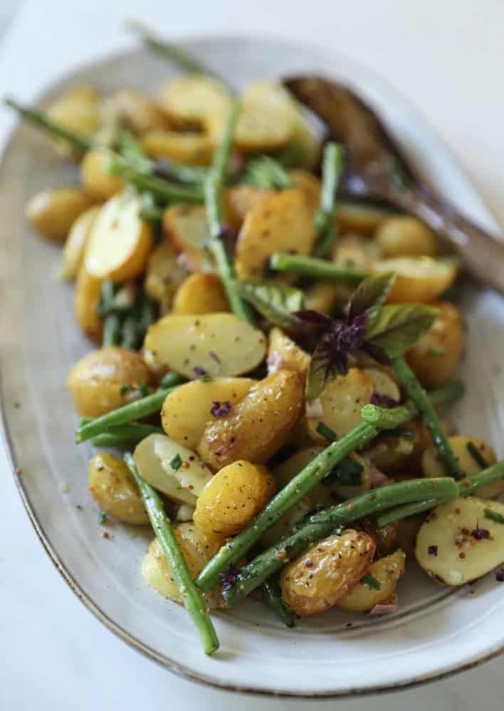 A platter of potato salad tossed with a vinaigrette, herbs , green beans and no mayo