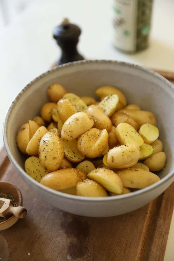 Sliced yukon gold potatoes in a bowl tossed with oil and seasonings.