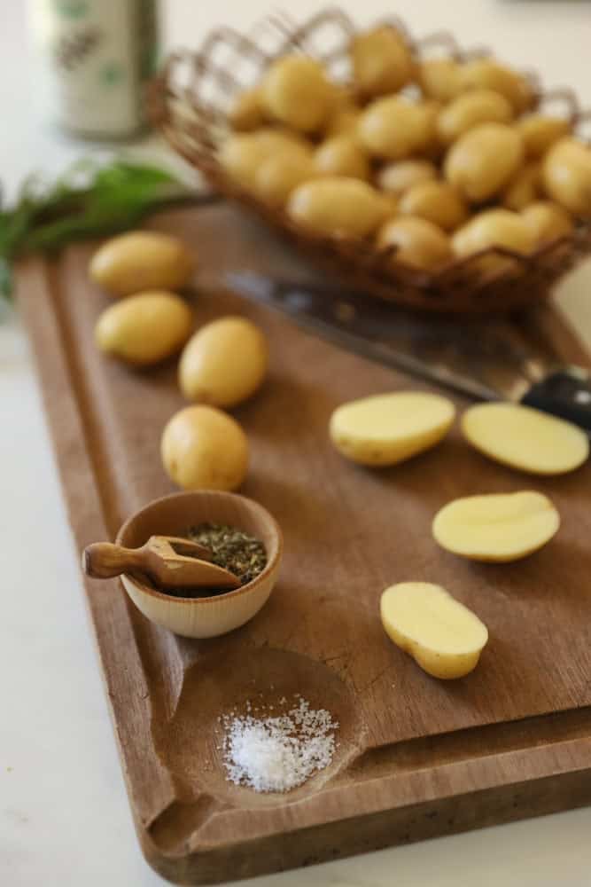 Sliced fingerling potatoes on a cutting board with salt and seasonings.