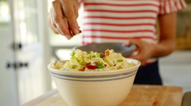 Adding a chopped bacon garnish to a bowl of potato salad