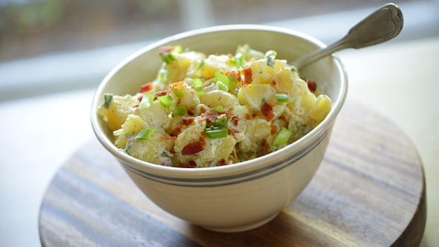 Close up of Traditional Potato Salad with bacon and green onions in bowl with a spoon