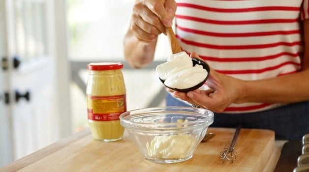 Adding sour cream and mayonnaise to mixing bowl to make potato salad