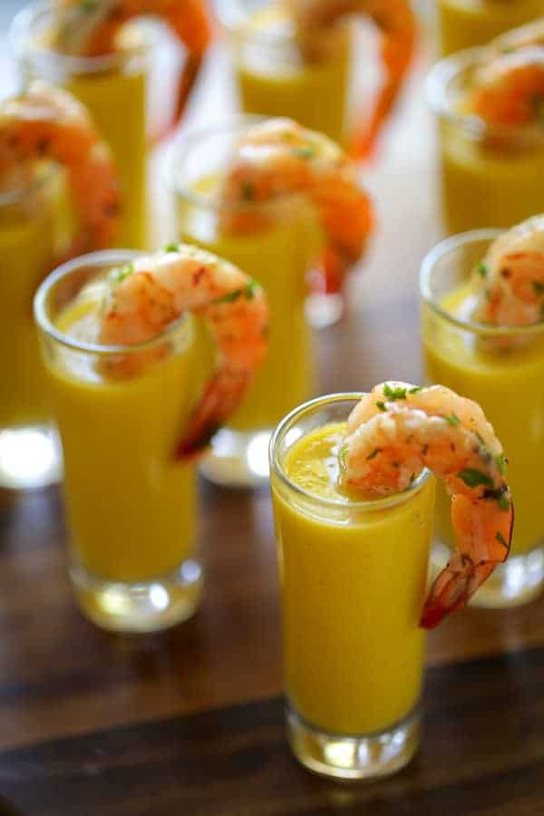 Vertical image of shot glasses filled with gazpacho soup and shrimp tails