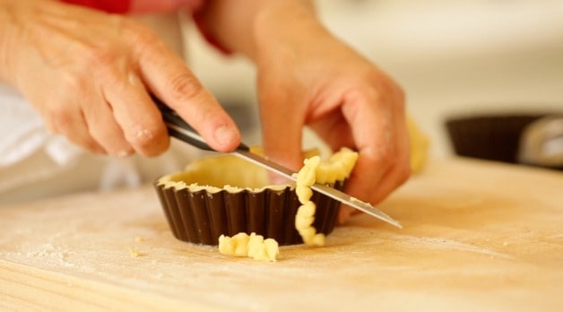 trimmen van de randen van het deeg voor recept van Kersenbakewell-taart