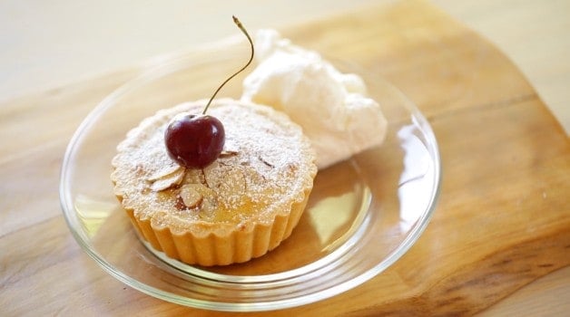 Cherry Bakewell tart with whipped cream on glass plate