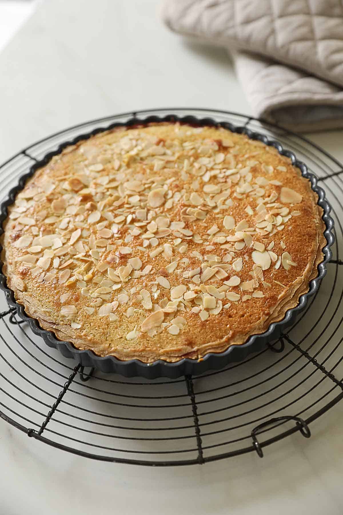 A baked cherry bakewell tart cooling on a wire rack.