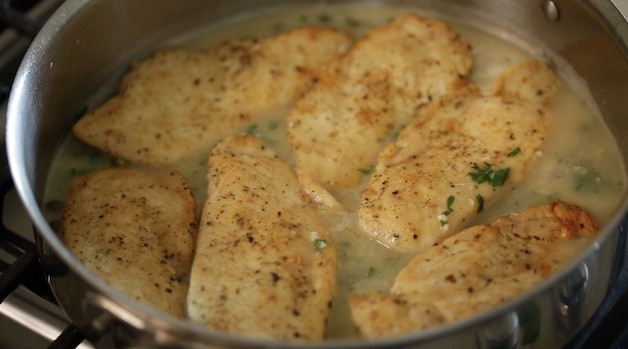 Placing seared chicken cutlets in skillet with the lemon caper sauce