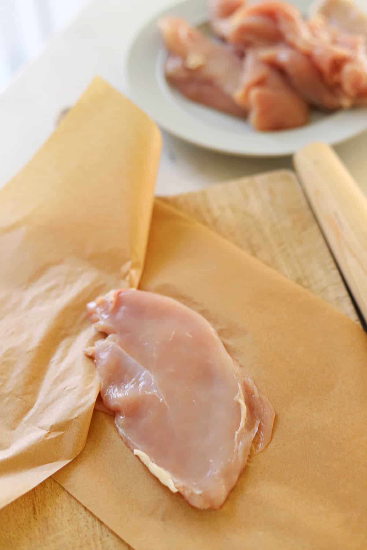 A pounded chick breast between parchment paper.